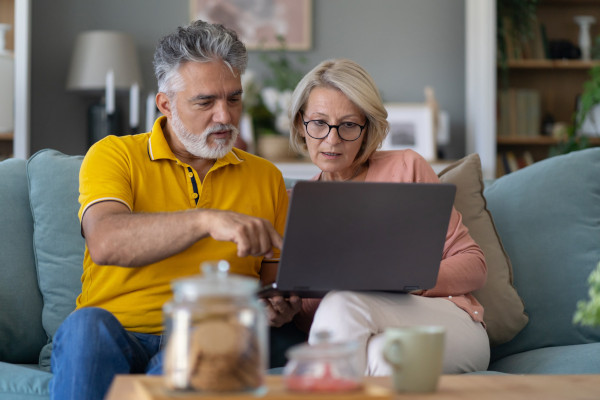 A senior couple using a laptop, sitting together on a sofa in a living room