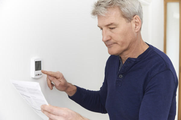 Mature Man Turning Down Heating Thermostat